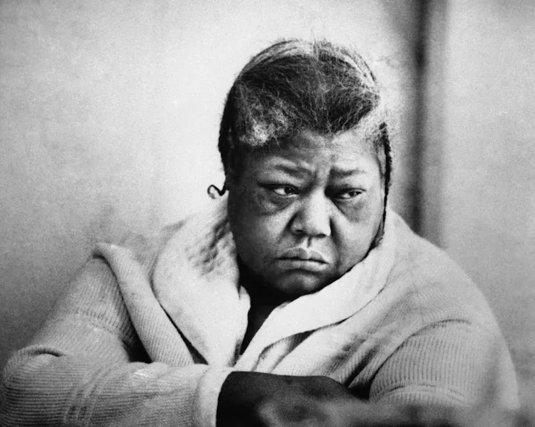 A Black woman wearing a bathrobe looks to her left with a serious expression.