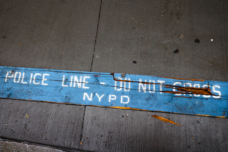A strip of blue barrier tape on the sidewalk reads 'POLICE LINE -- DO NOT CROSS NYPD'