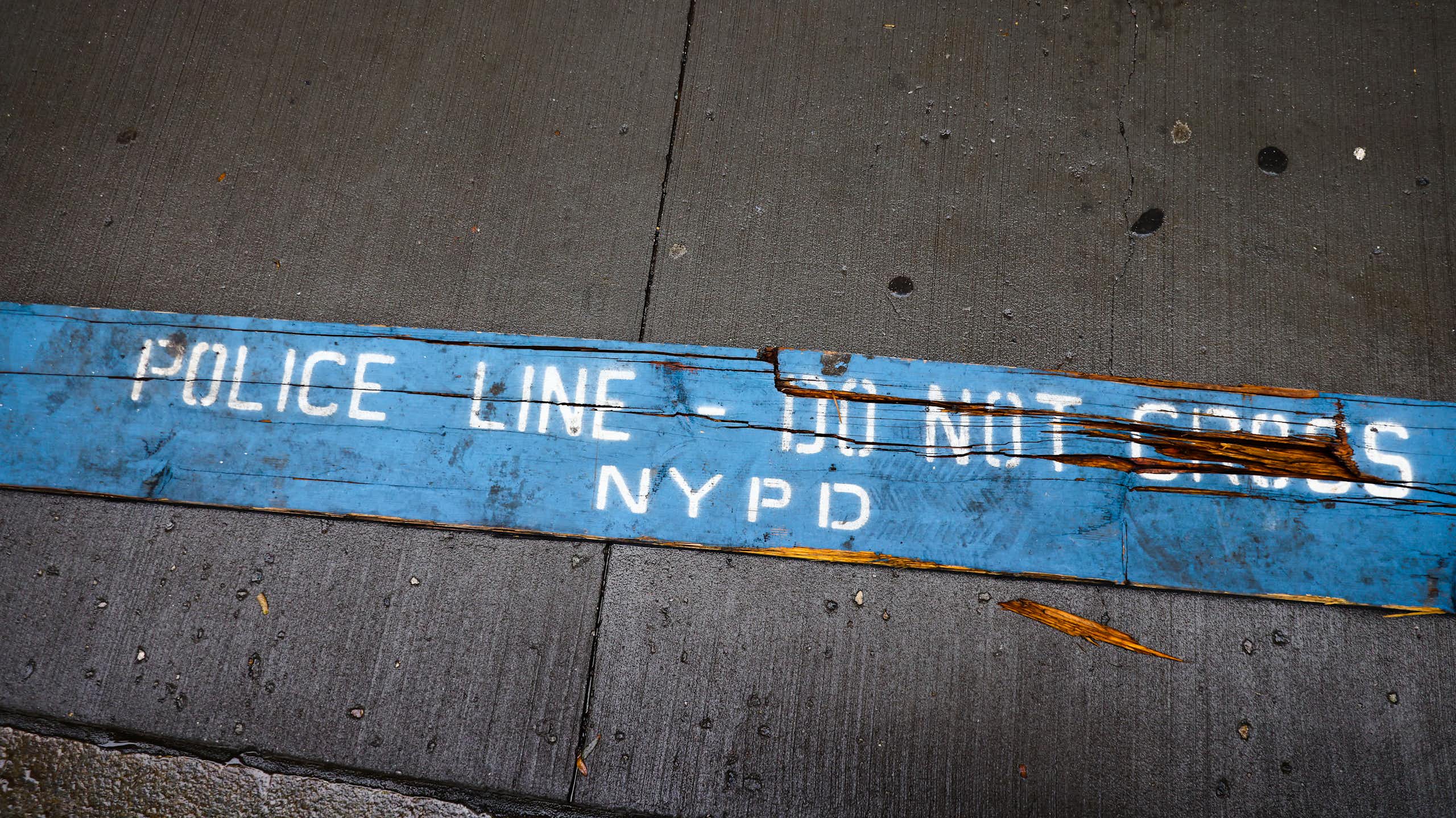 A strip of blue barrier tape on the sidewalk reads 'POLICE LINE -- DO NOT CROSS NYPD'