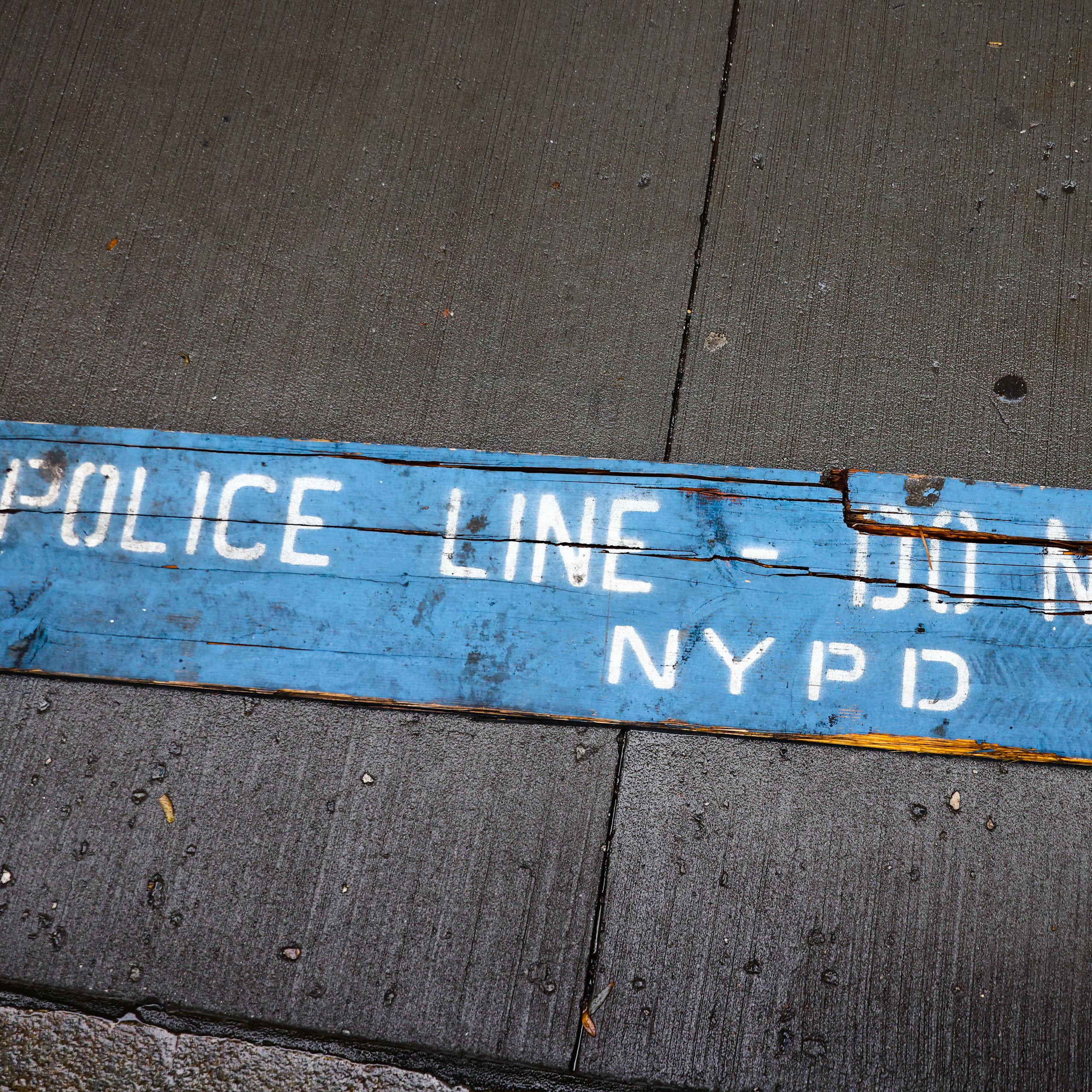 A strip of blue barrier tape on the sidewalk reads 'POLICE LINE -- DO NOT CROSS NYPD'