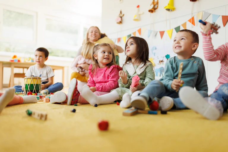 A row of children sit and play in a daycare classroom.