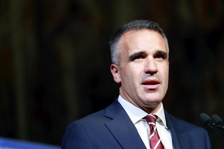 A man in a suit speaks in front of a dark background
