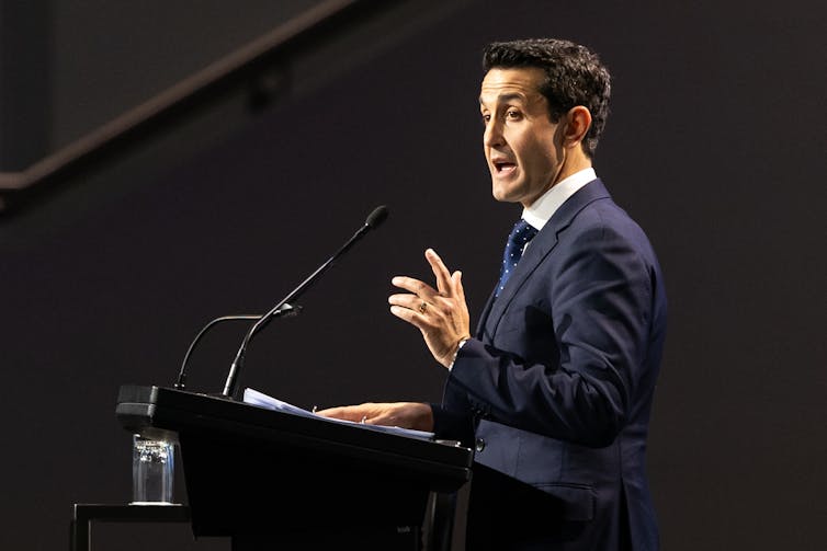 A man in a suit at a lectern speaks to an audience