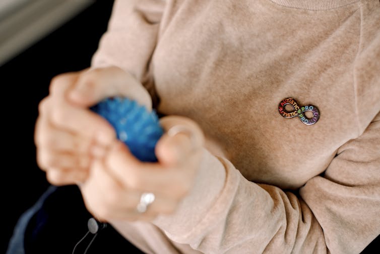 A close-up of an infinity shape brooch on the sweater of an adult who is squeezing a stress ball.
