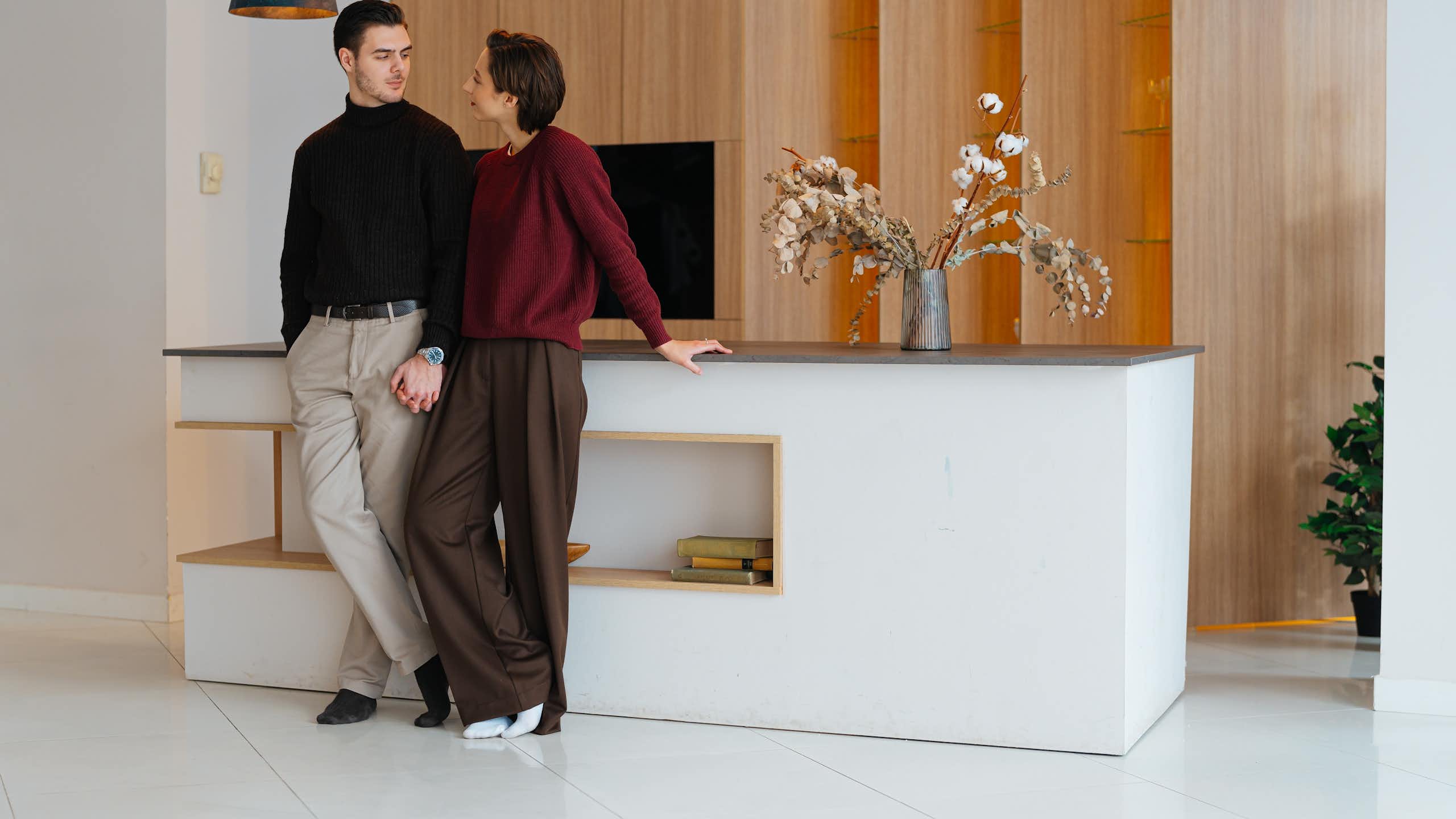 Two adults appear to be looking into each other’s eyes while standing next to each other in an elegant, sparsely furnished room.