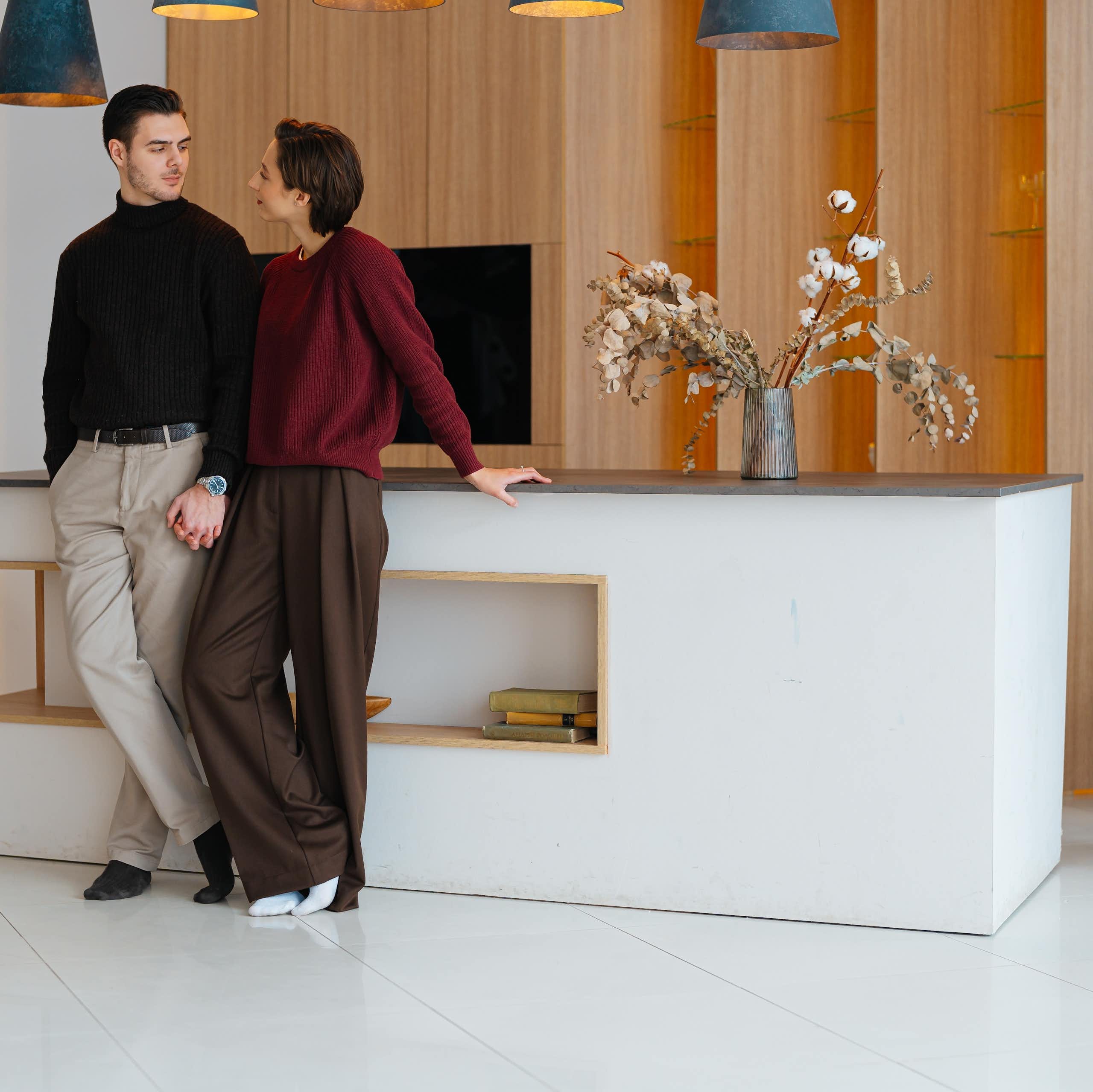 Two adults appear to be looking into each other’s eyes while standing next to each other in an elegant, sparsely furnished room.