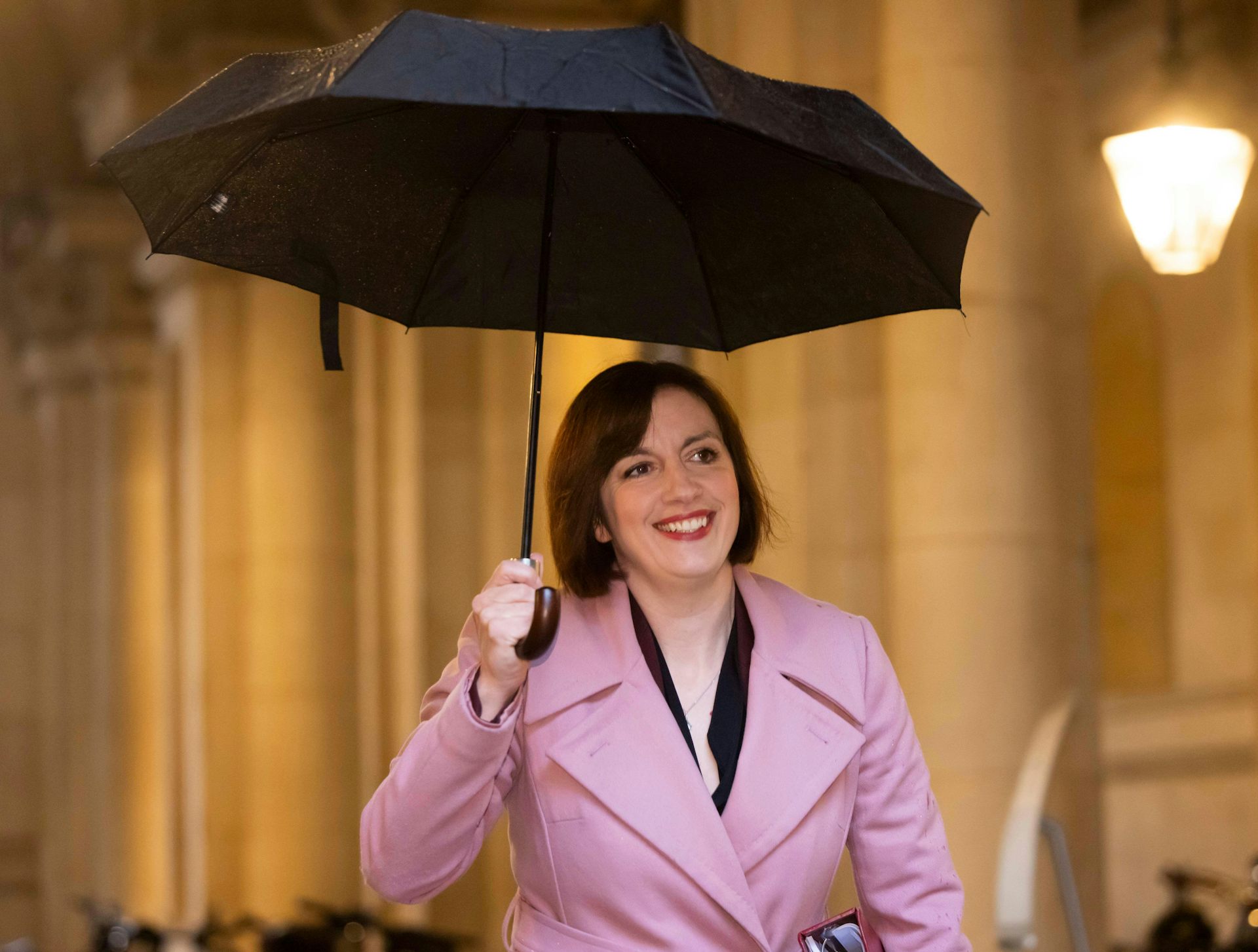 Bridget Phillipson smiling and walking holding an umbrella