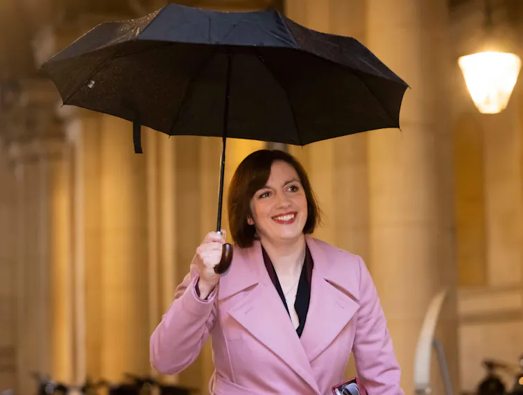 Bridget Phillipson smiling and walking holding an umbrella