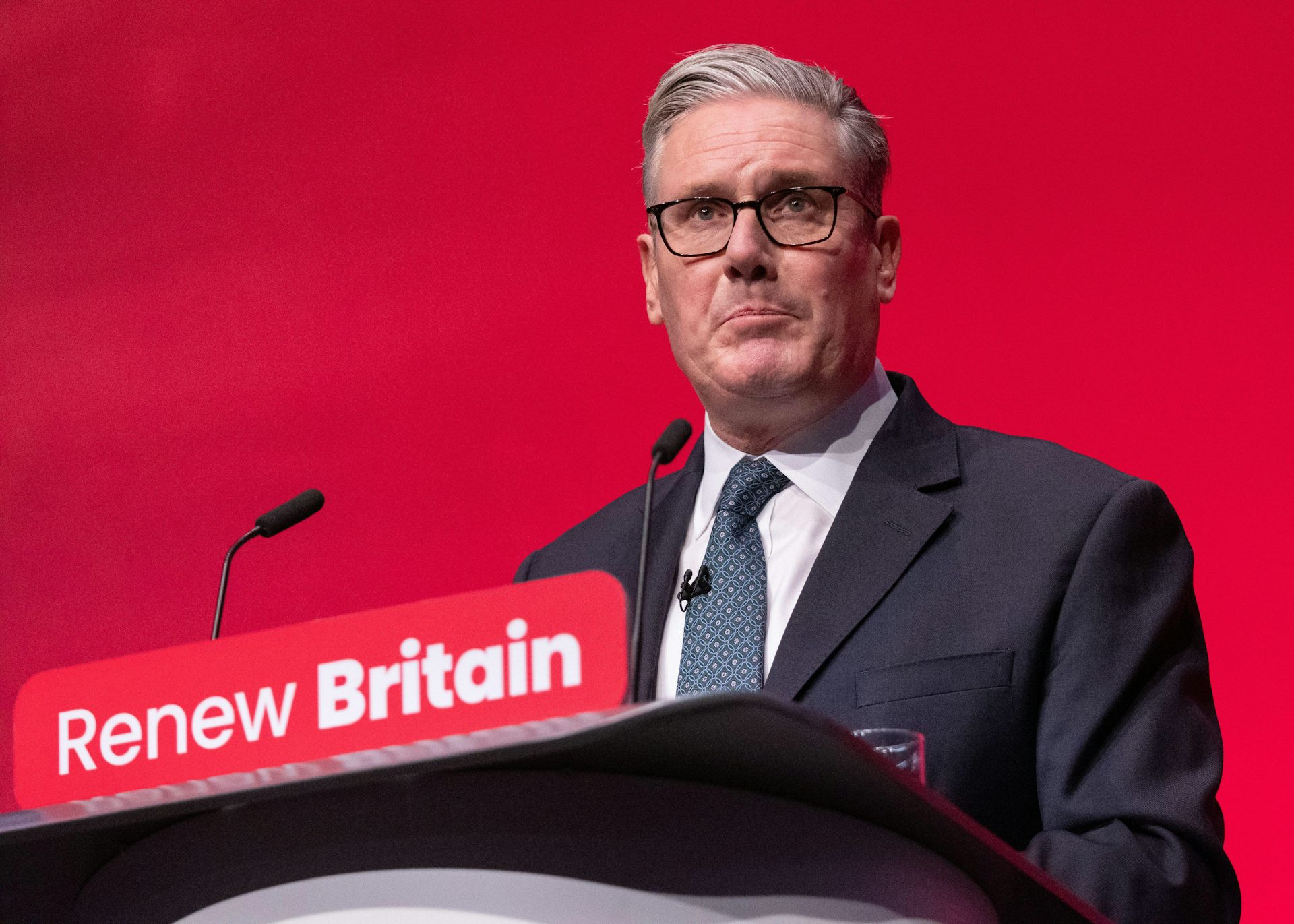 Keir Starmer appearing behind a red background frowning