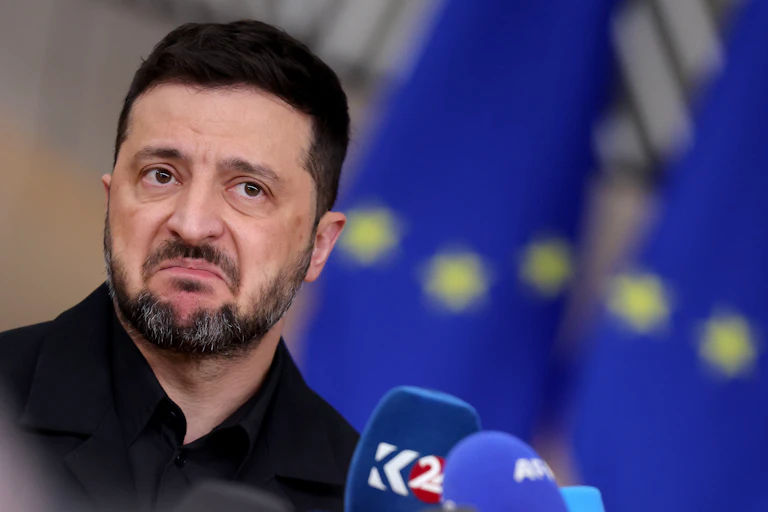 Ukraine's president, Volodymyr Zelensky, frowning, In the background are EU flags.