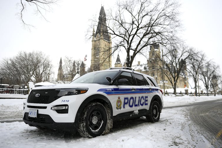 Un coche patrulla de la policía se encuentra en una calle nevada con los edificios del parlamento al fondo.