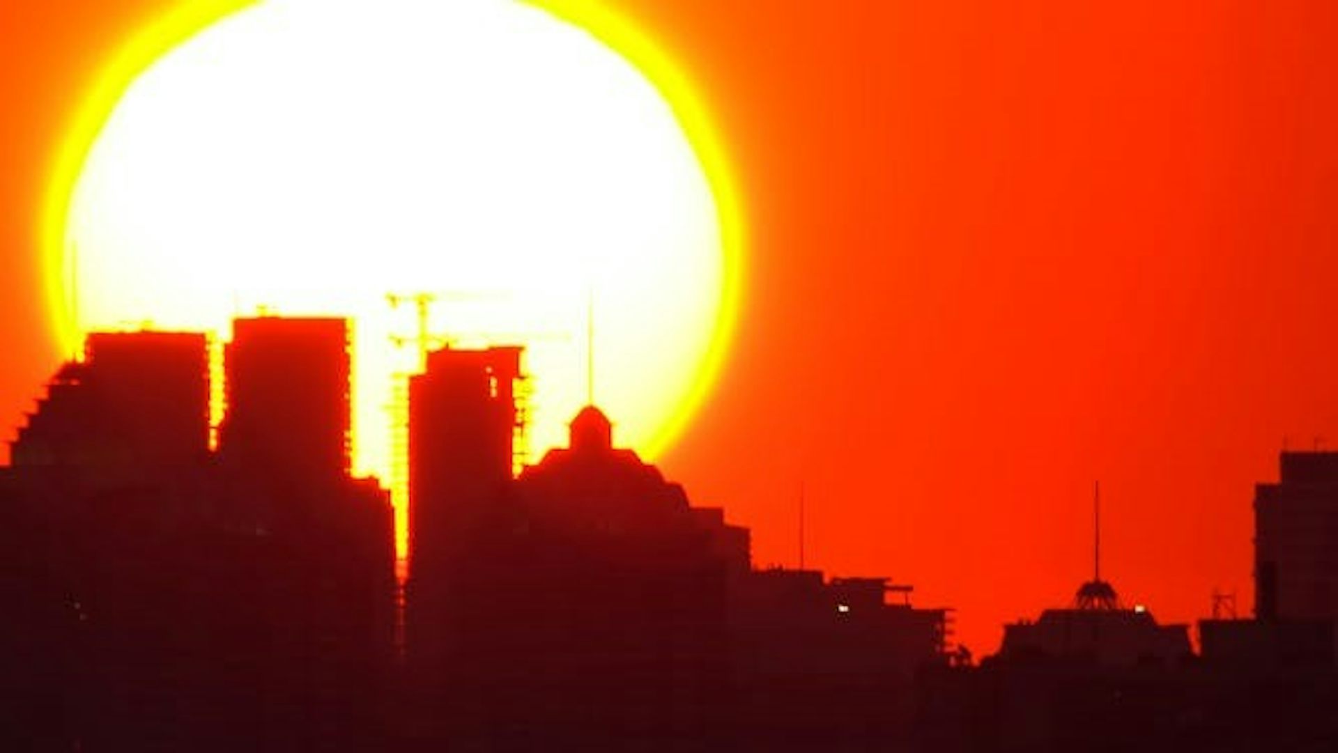 Silhouette d’une ville sous un soleil brûlant et un ciel orangé.