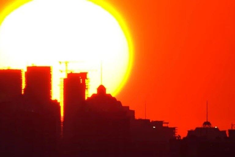 Silhouette d’une ville sous un soleil brûlant et un ciel orangé.
