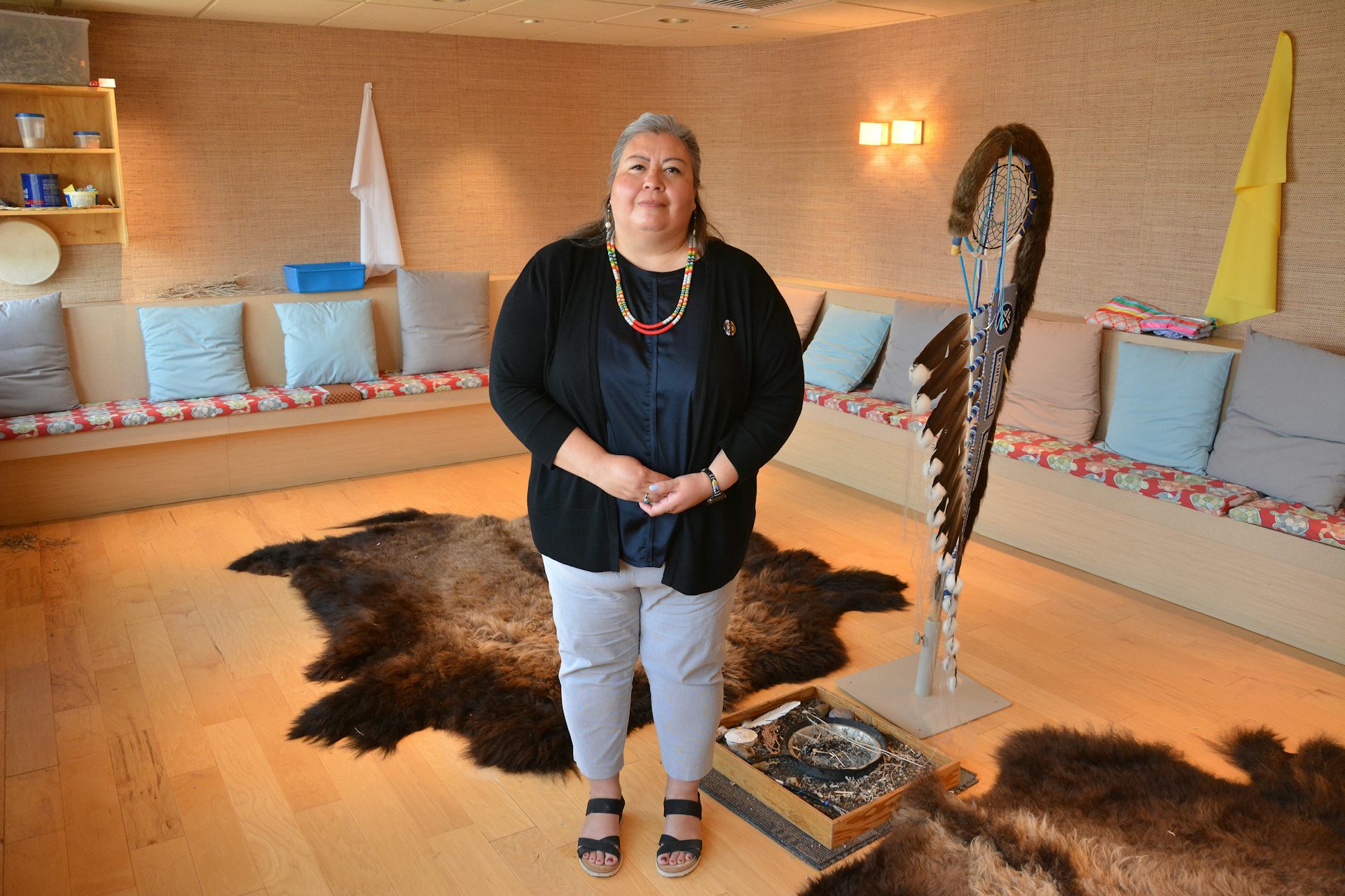 Un hombre se encuentra en una habitación con cojines, bancos y pieles en el suelo.