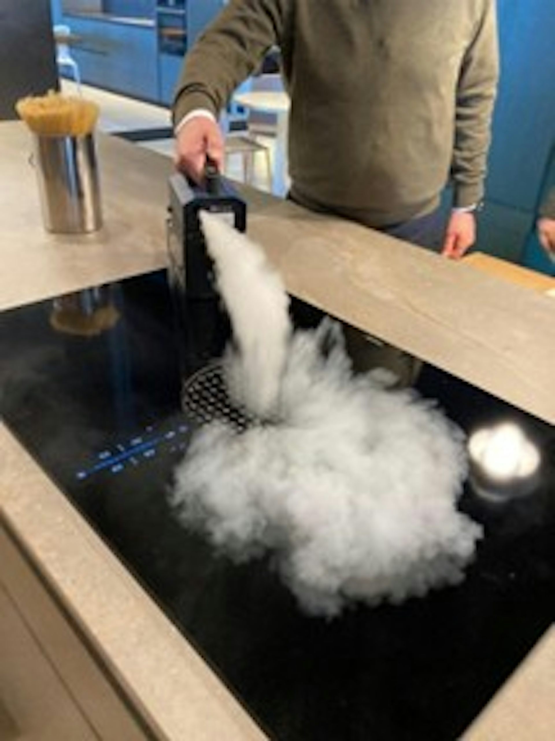 A person sprays smoke on a hood built into a kitchen countertop