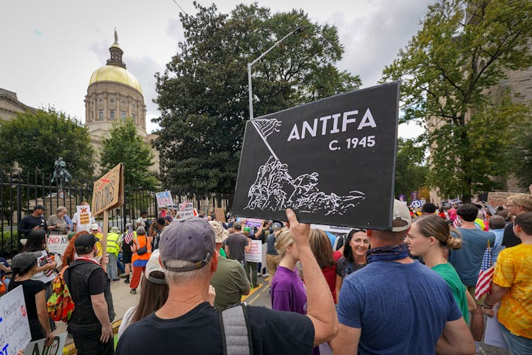 Protesters, some holding signs, walk toward a building with a dome.