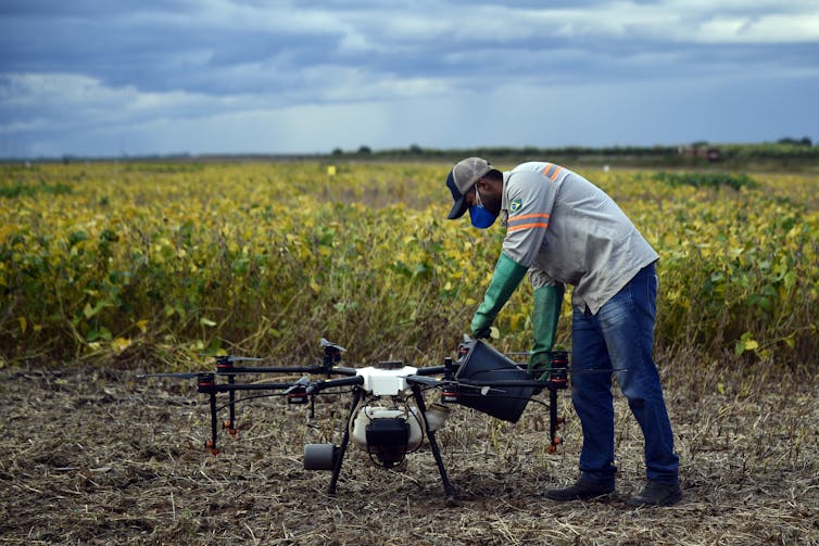 A person pours liquid into a tank attached to a drone, while standing near a large field.