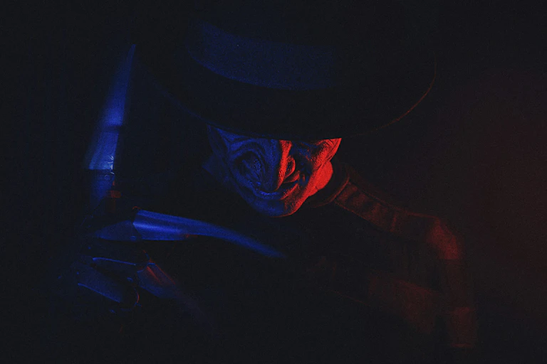 An image of a man wearing a hat and a glove with sharp blades on his right hand.