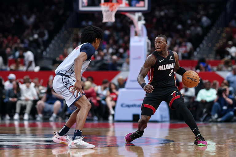 Basketball player in a red and black jersey dribbles while being guarded by a player in a white jersey.