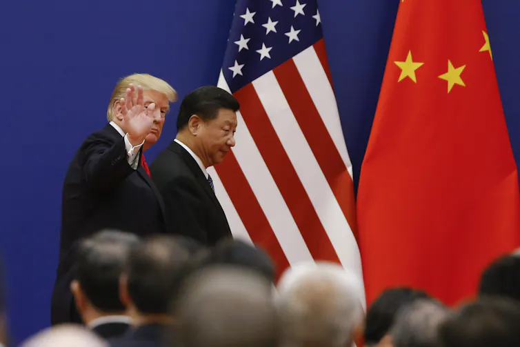 Two men walk side by side in front of large flags.