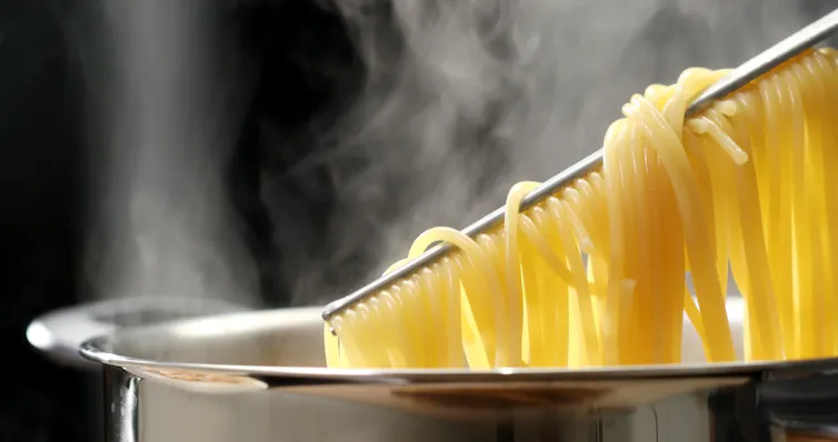 Spaghetti is taken out of the pan with tongs
