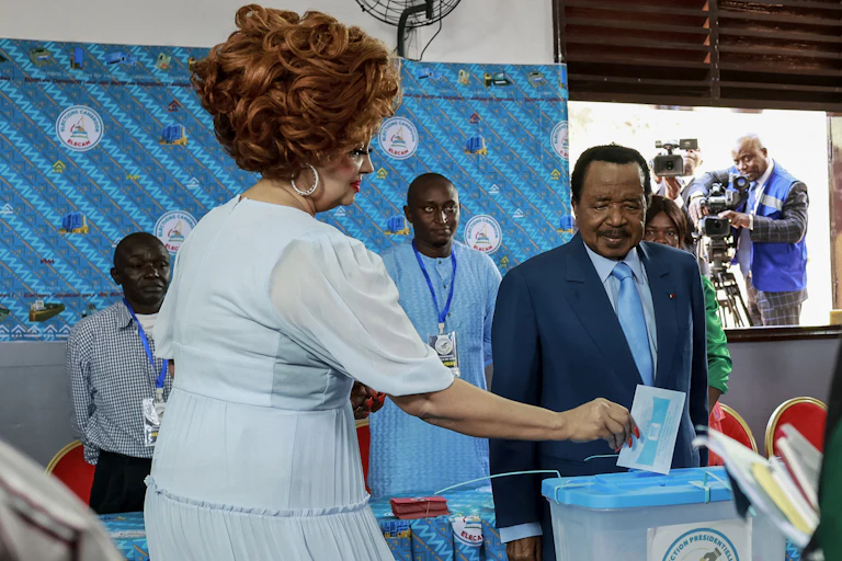 A woman casting her ballot while a man in blue suit looks