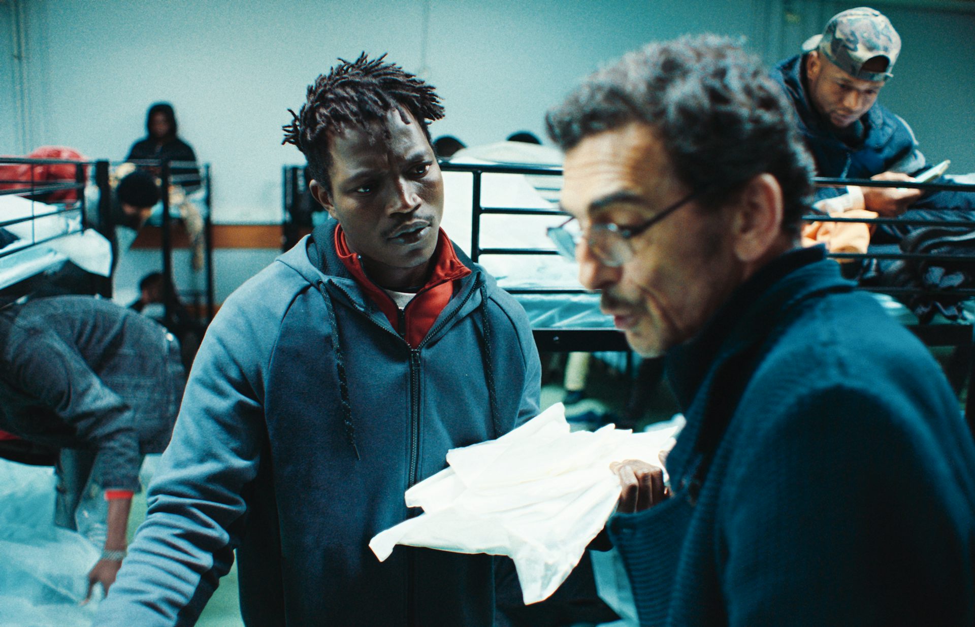 A young black man talking to an older white man holding a sheaf of papers.