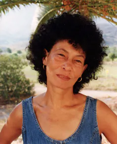 A woman with a large Afro looks to camera, unamused.
