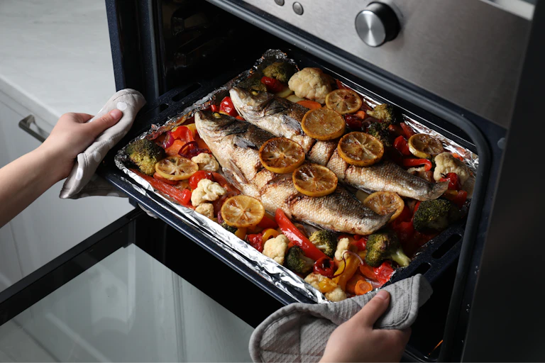 Unas manos sacan del horno una bandeja con pescado y verduras