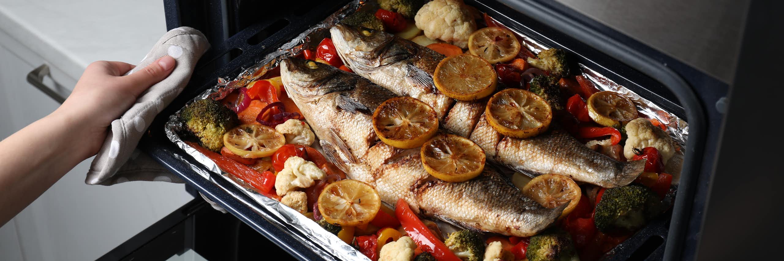 Unas manos sacan del horno una bandeja con pescado y verduras