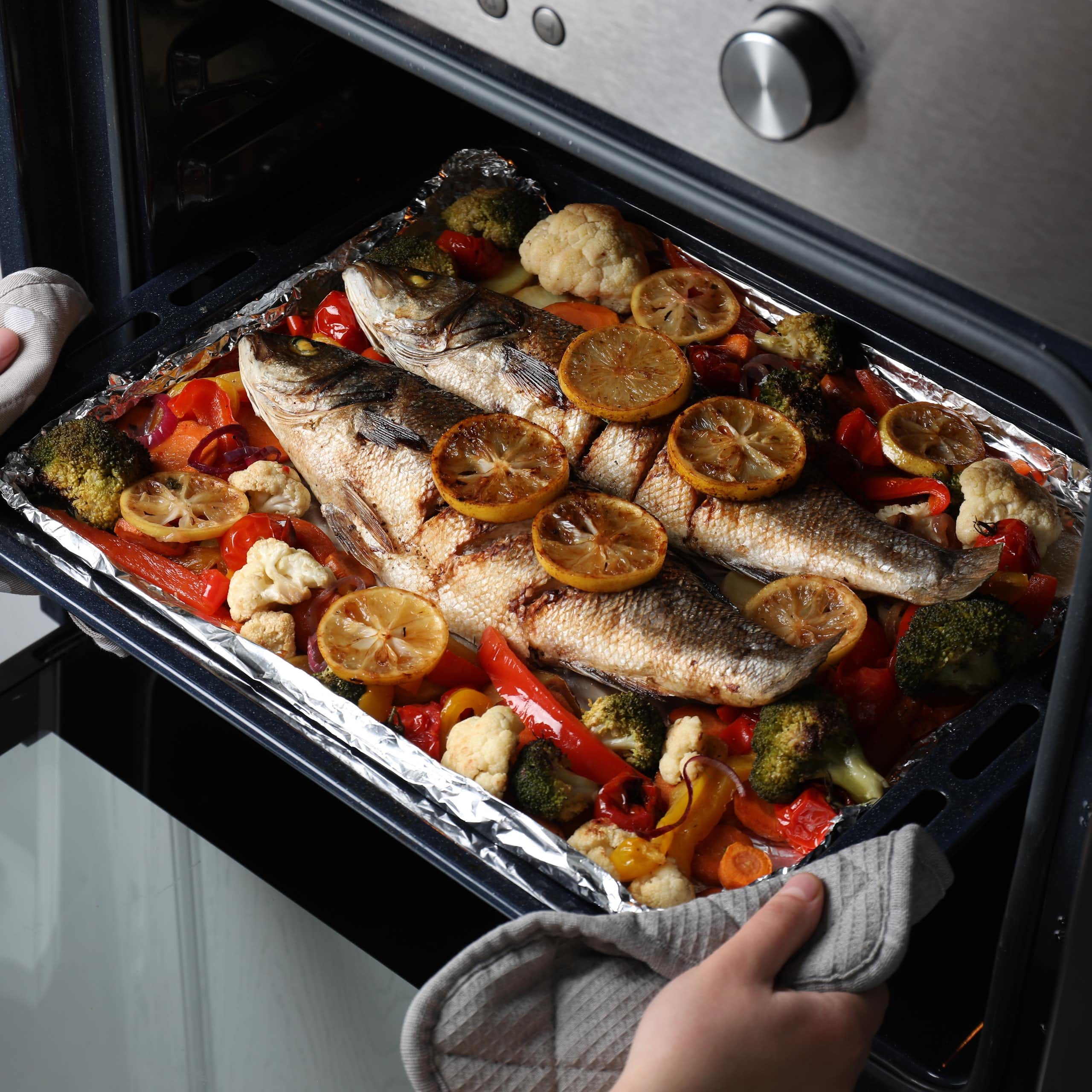 Unas manos sacan del horno una bandeja con pescado y verduras