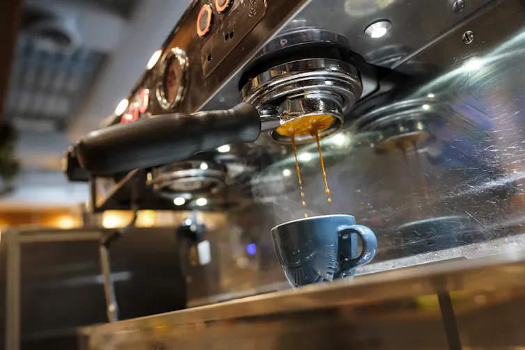 espresso falls from a coffee machine into a blue cup