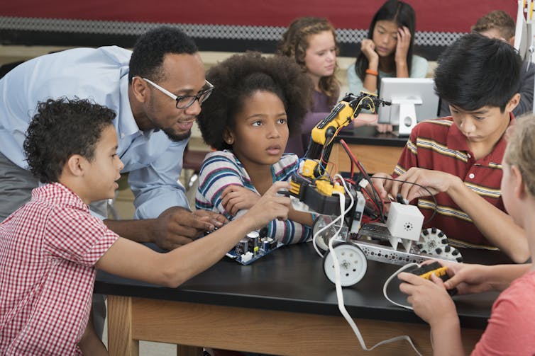 Middle school students work on a robotics project with a teacher