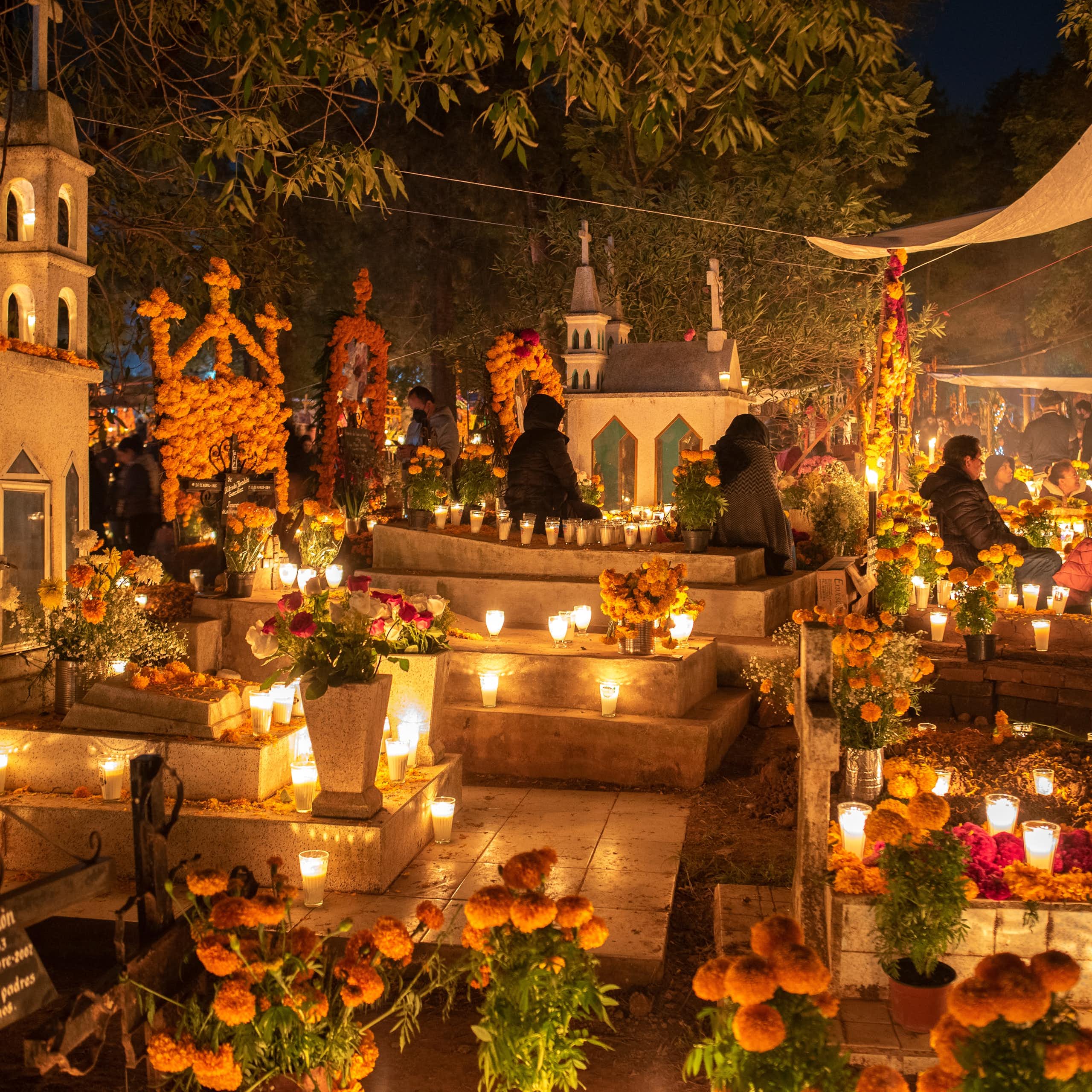 Un cementerio de noche con velas y adornos florales.