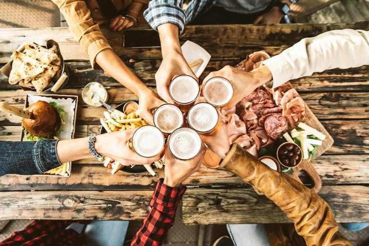 People raising beer glasses at a wooden table covered with food