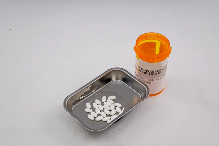 An orange pill bottle with a label that says atorvastatin next to a small metal tray containing pills.