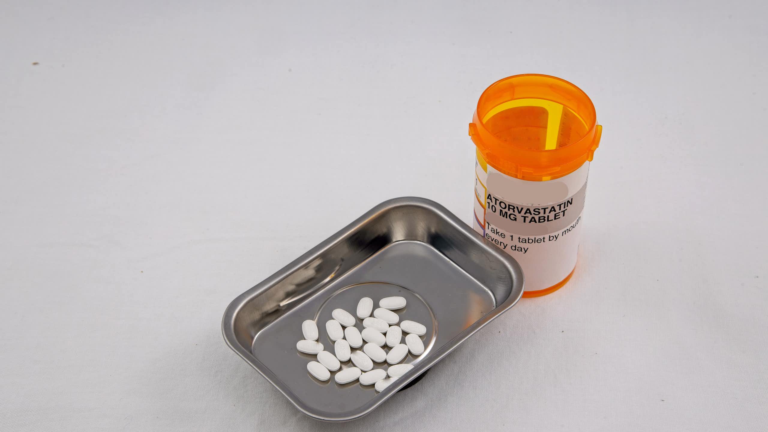 An orange pill bottle with a label that says atorvastatin next to a small metal tray containing pills.