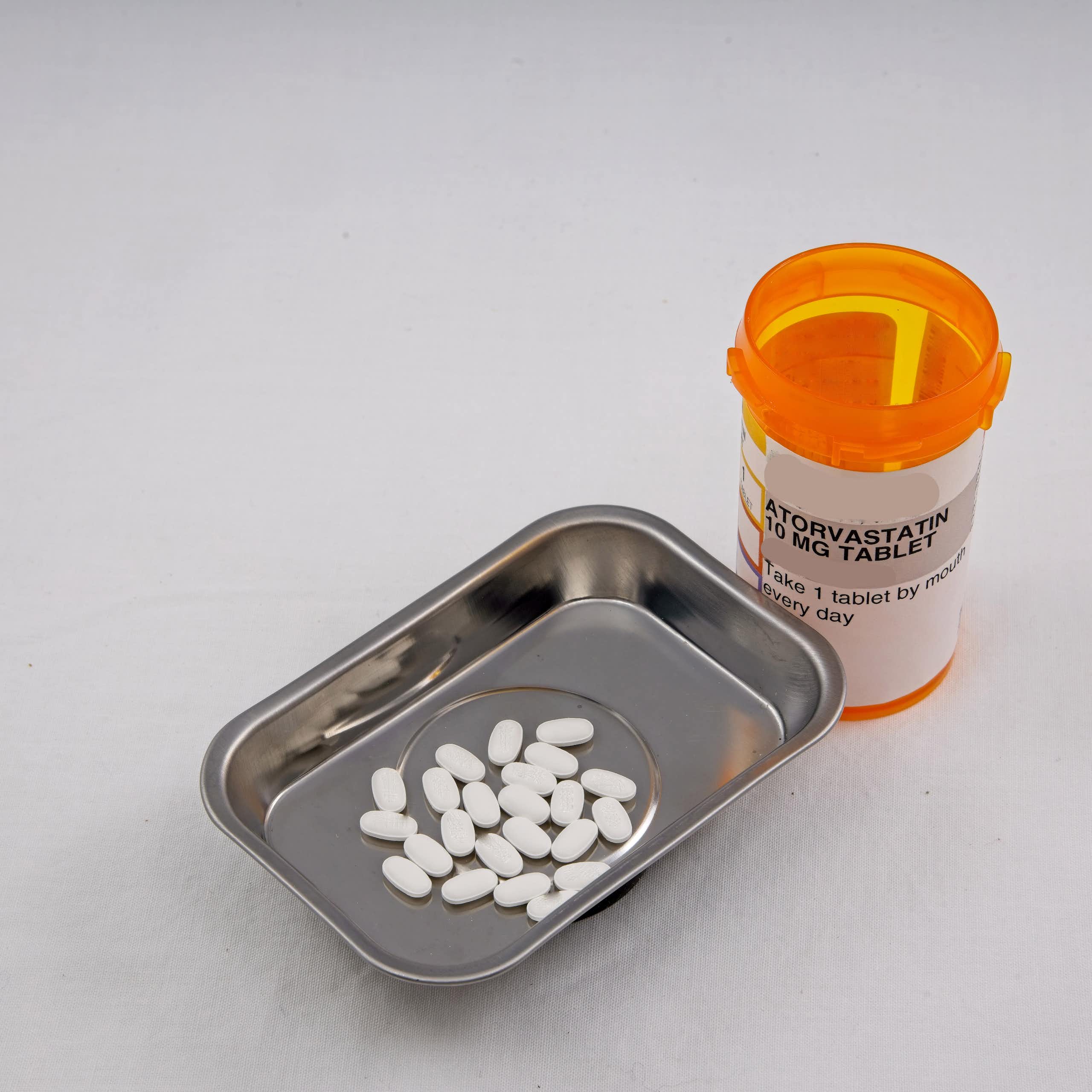 An orange pill bottle with a label that says atorvastatin next to a small metal tray containing pills.