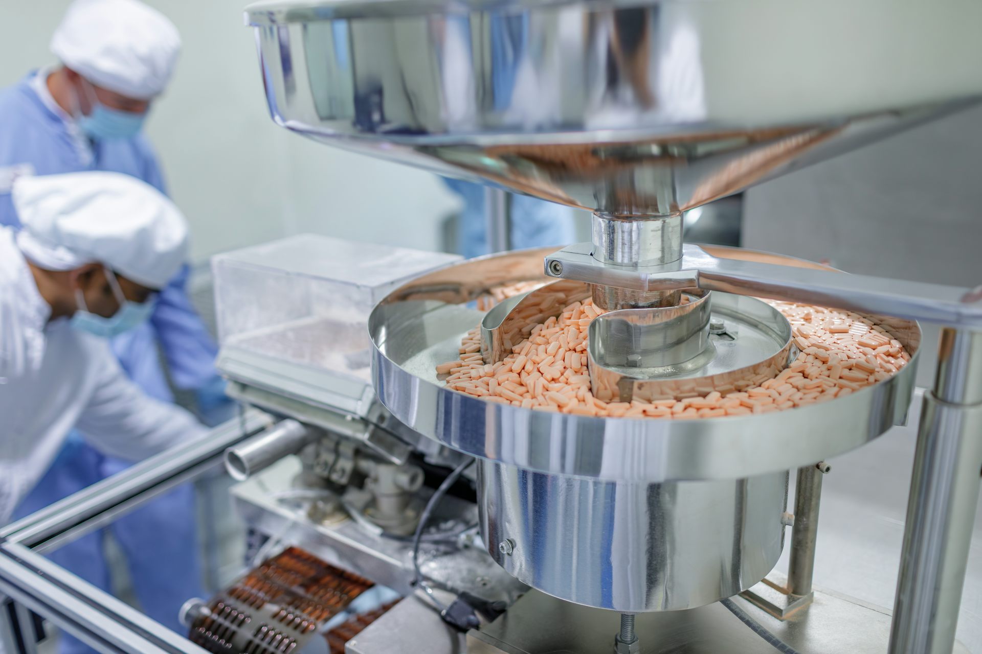 Two people operating a tablet production line at a pharmaceutical manufacturing facility