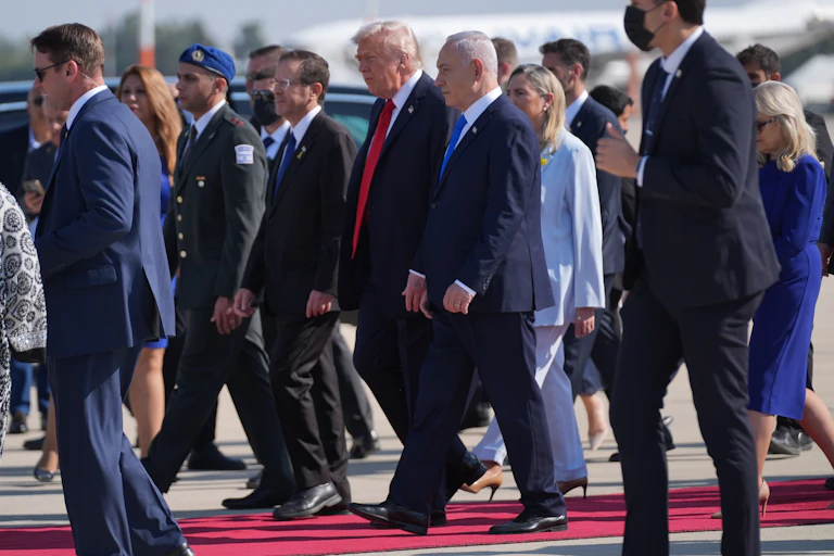 A man in a suit and red tie walks next to a man in a suit and blue tie.