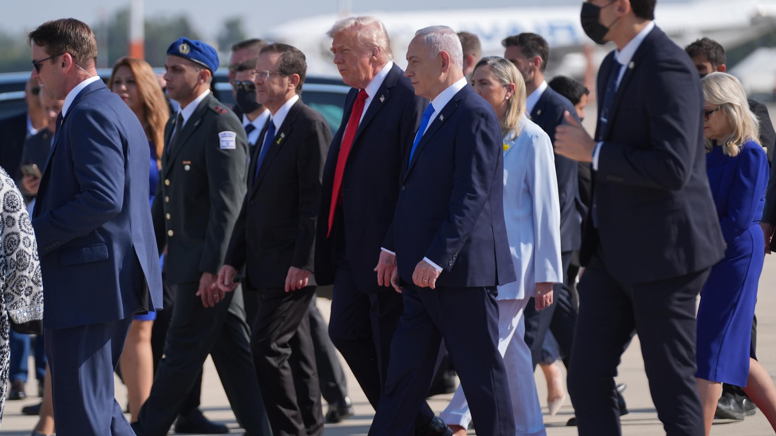 A man in a suit and red tie walks next to a man in a suit and blue tie.