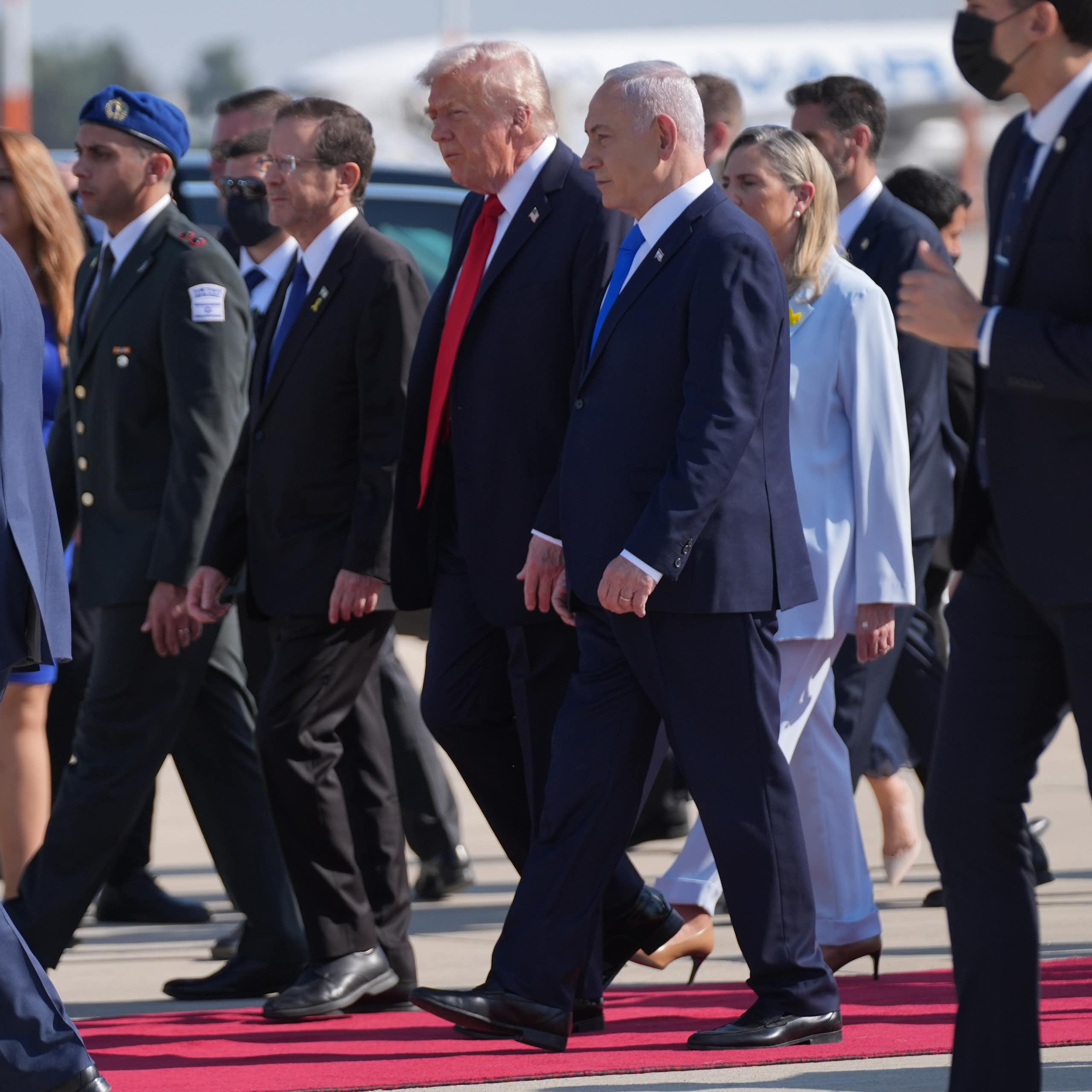 A man in a suit and red tie walks next to a man in a suit and blue tie.
