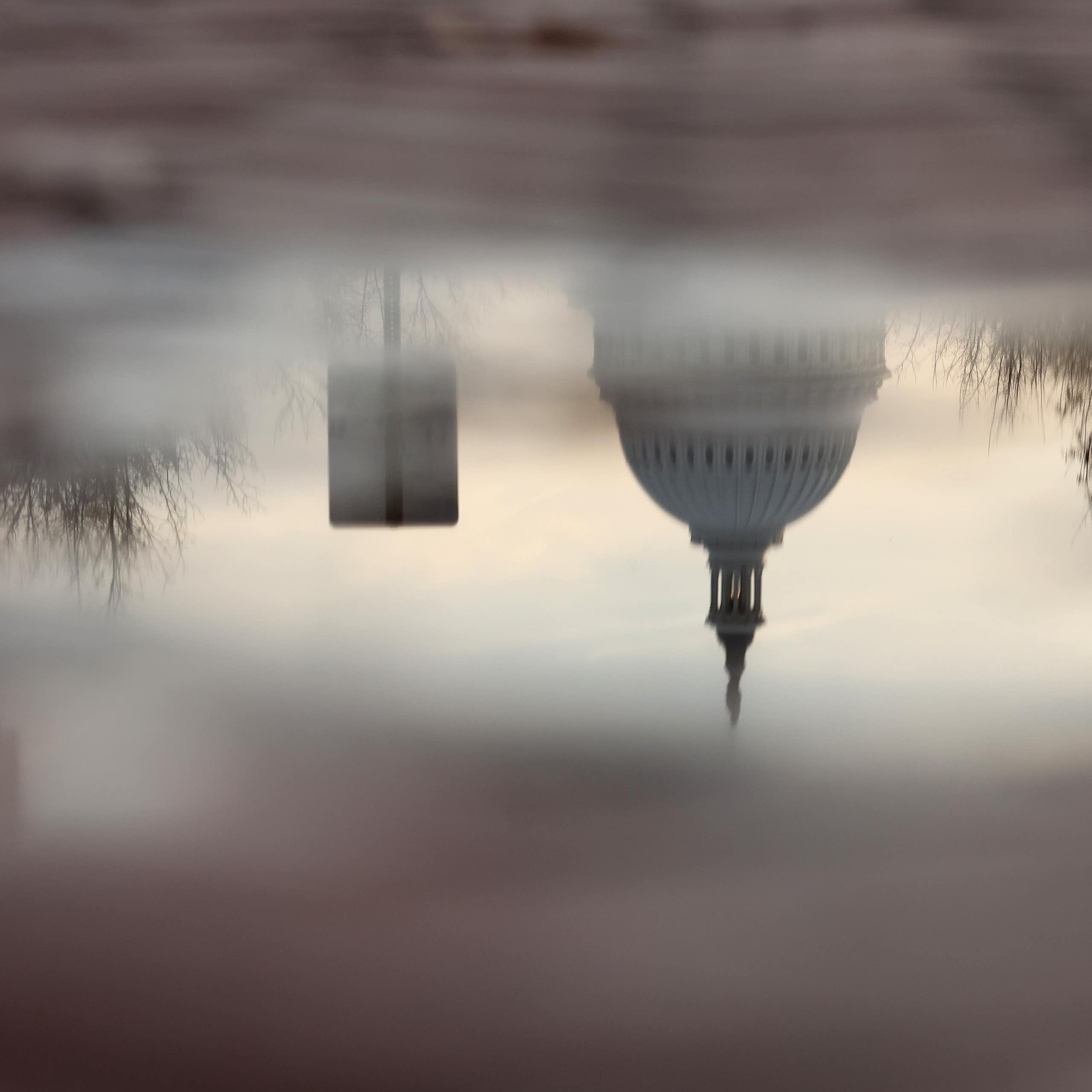 The U.S. Capitol is seen in the reflection of a puddle.