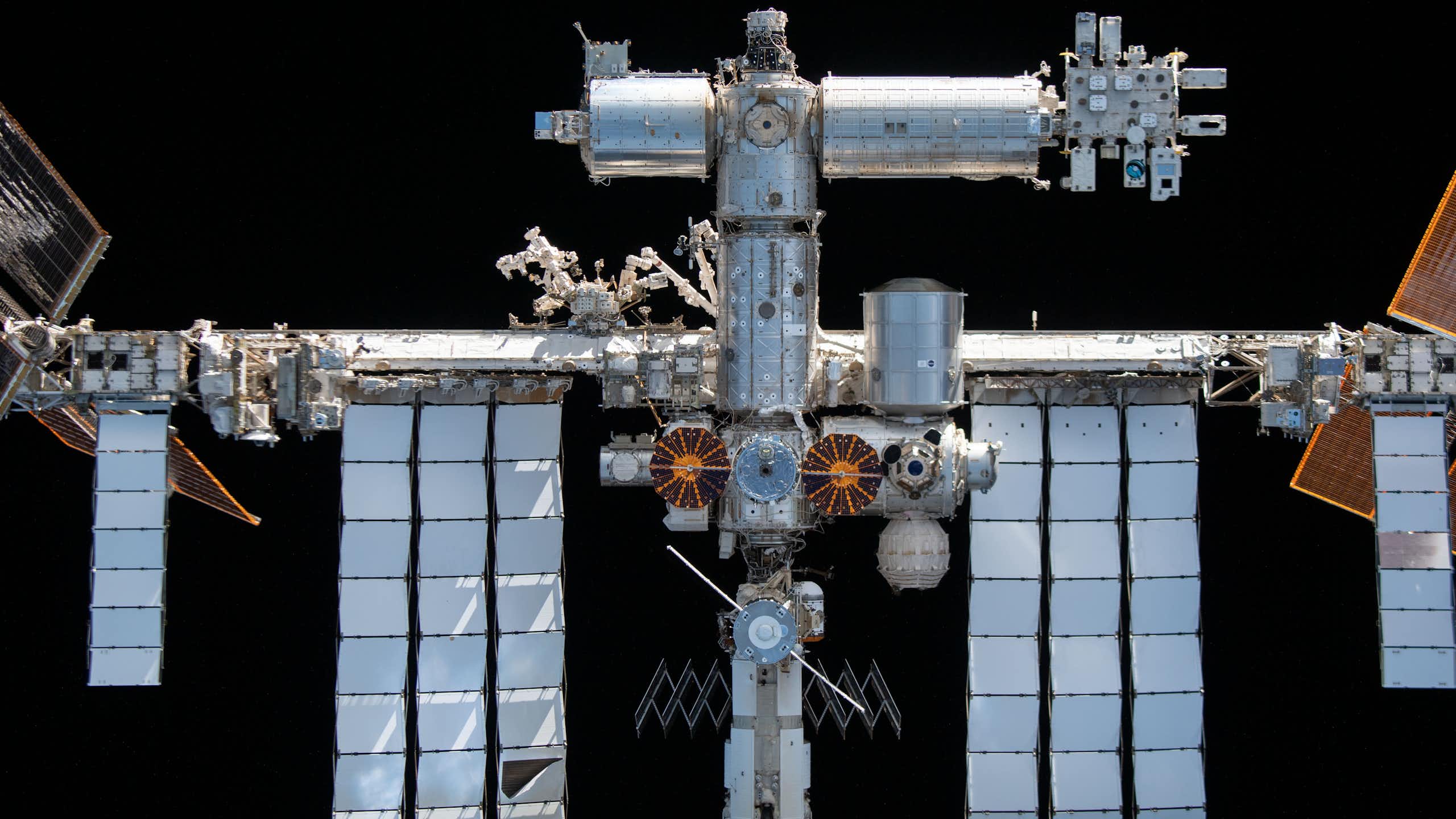 Silver modules of a space station, with a truss extending to the sides holding huge solar panel arrays. The station is completely surrounded by blackness.