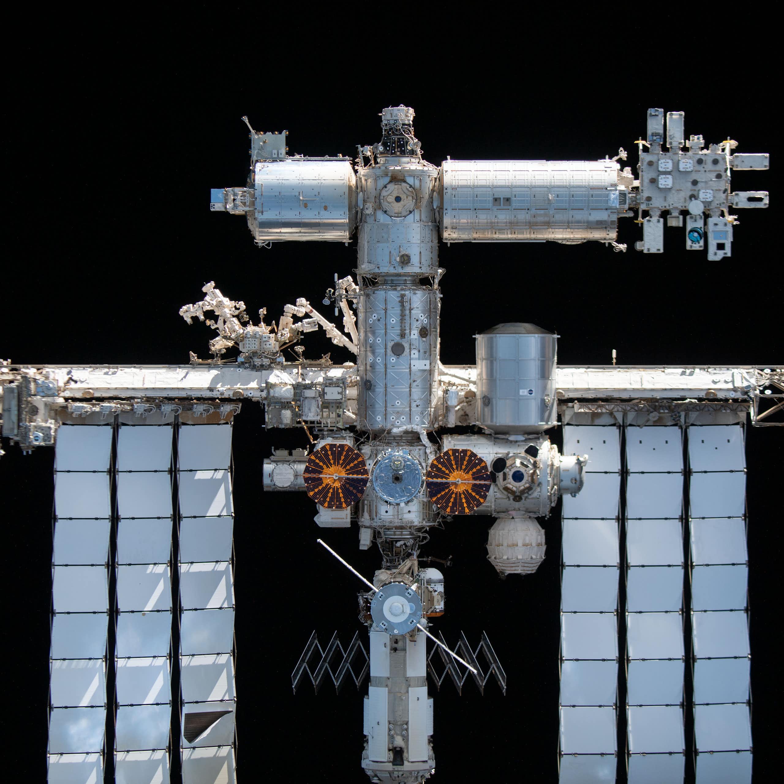 Silver modules of a space station, with a truss extending to the sides holding huge solar panel arrays. The station is completely surrounded by blackness.