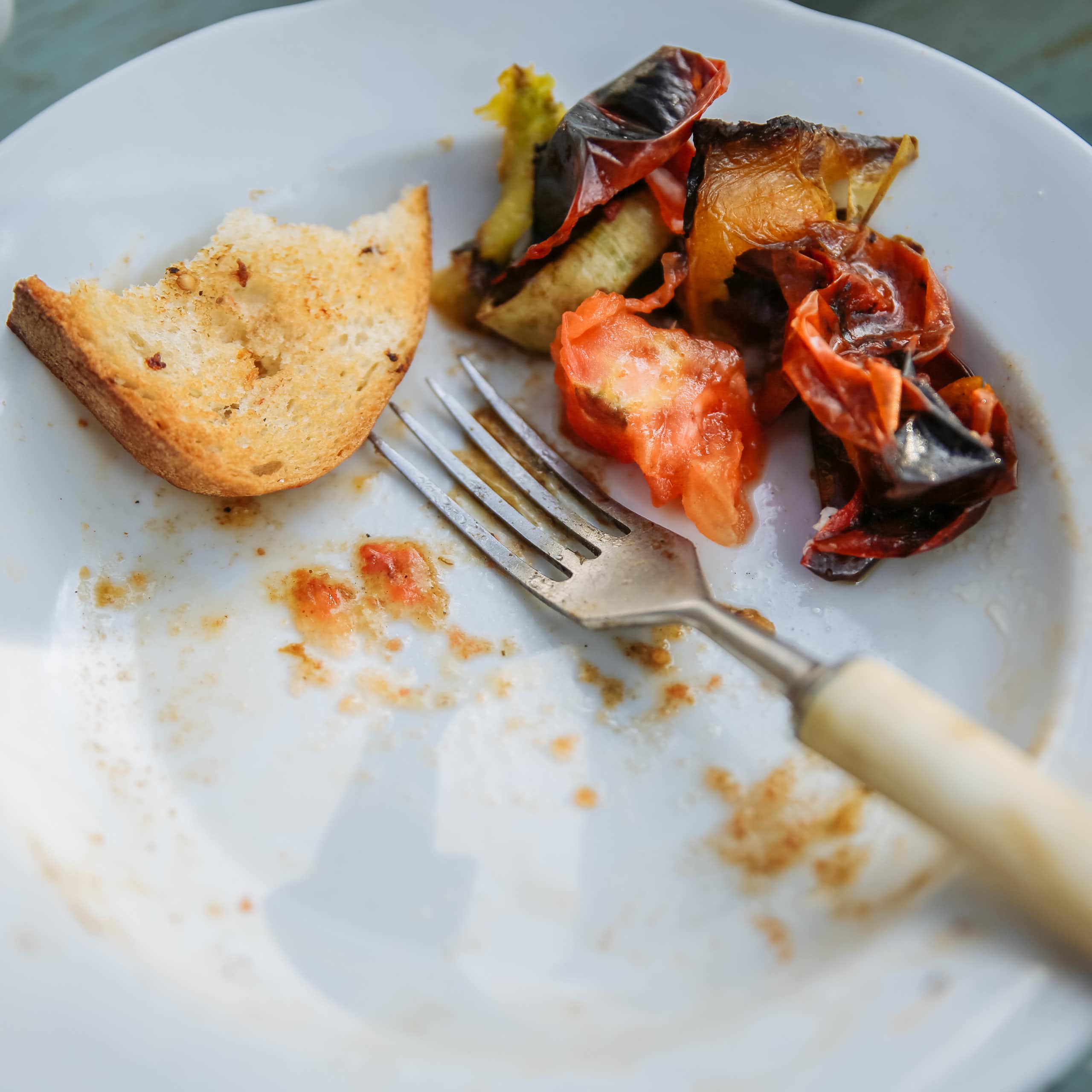 A white plate with a few bites of bread and vegetables leftover.