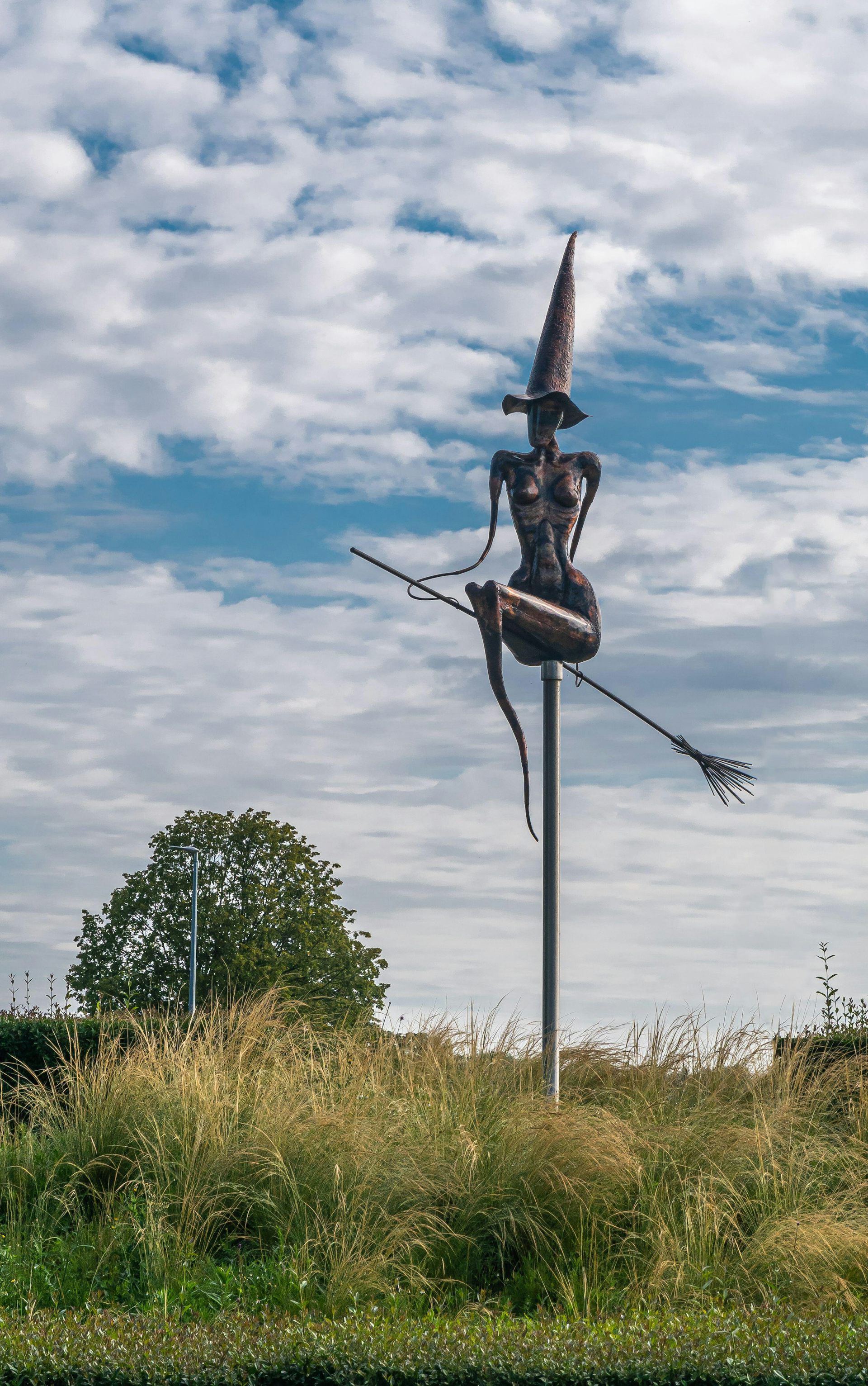 A statue of a naked witch on a broomstick with a pointy hat.