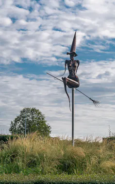 A statue of a naked witch on a broomstick with a pointy hat.