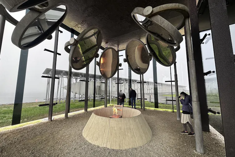 An artwork featuring a ring of mirrors hanging over a chair burning within a enclosed concrete circle.