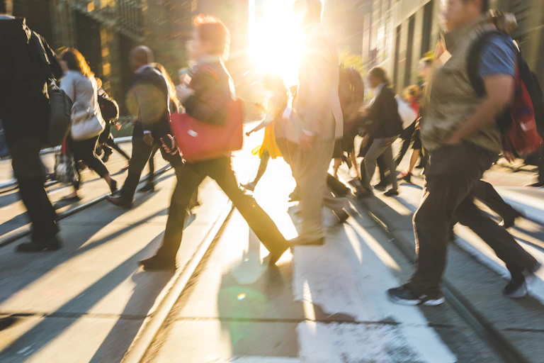 blurred shot of commuters crossing a street as the sun sets.